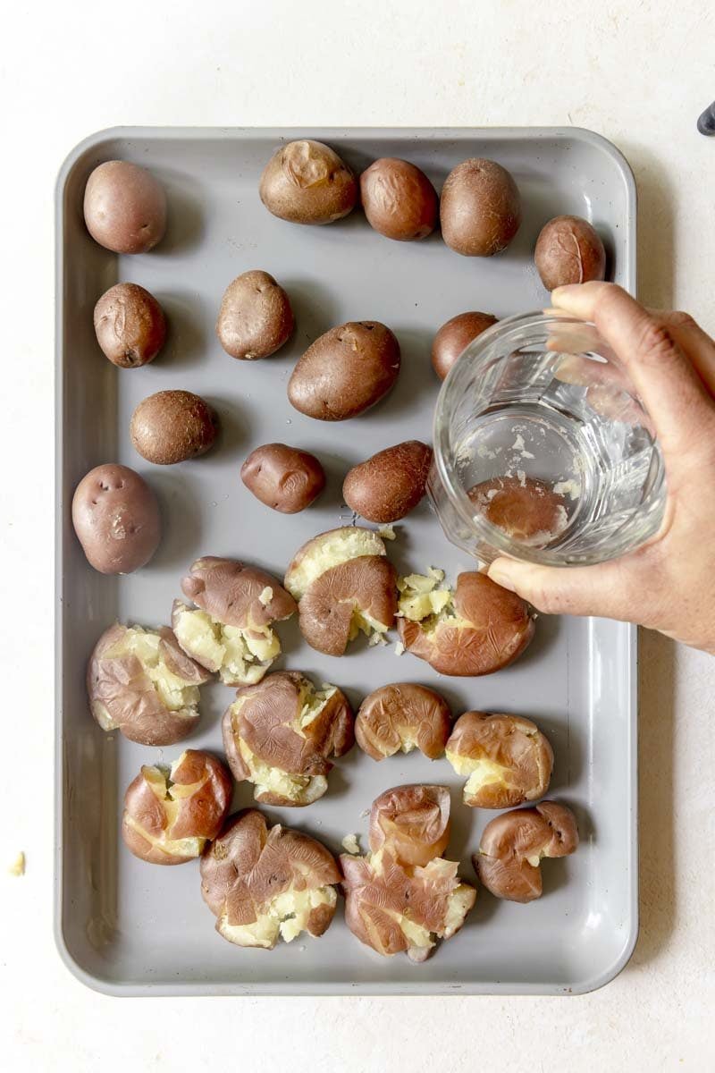 Smashing the cooked red potatoes with the bottom of a cup.