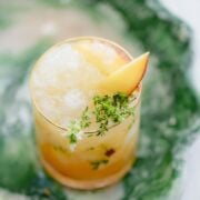 Peach Bourbon Smash with Thyme and Honey on a green tray.