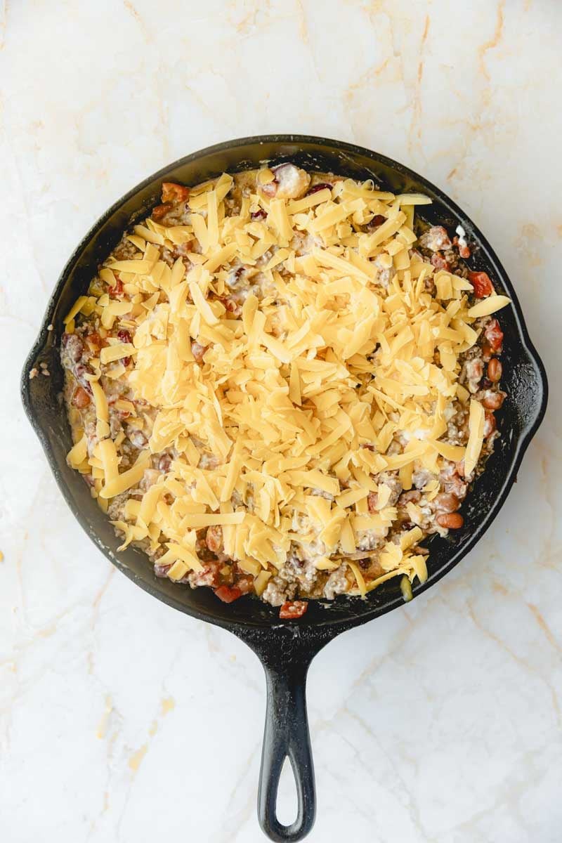 Cheese on top of the uncooked chili dip in a cast iron skillet. 