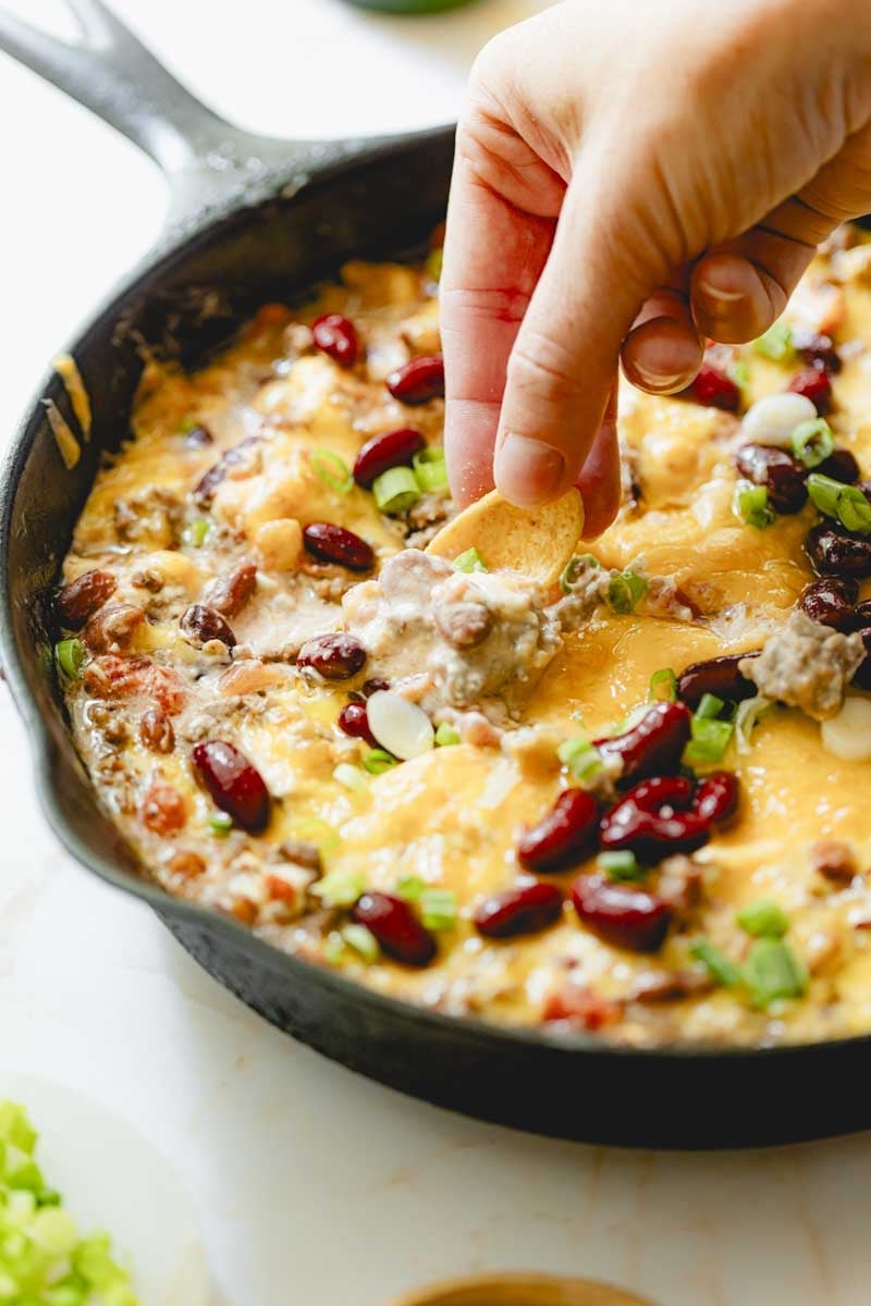 Dipping a corn chip into cooked chili cheese dip. 