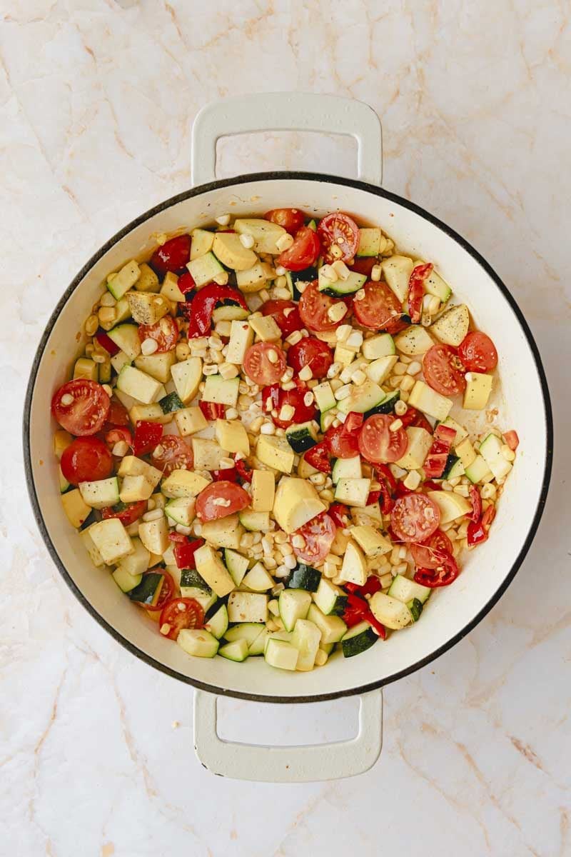 Sautéing garlic, peppers, zucchini, corn and tomatoes in olive oil in a large skillet.