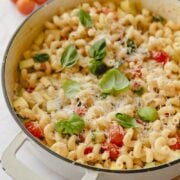 White skillet of creamy vegetable pasta garnished with basil.