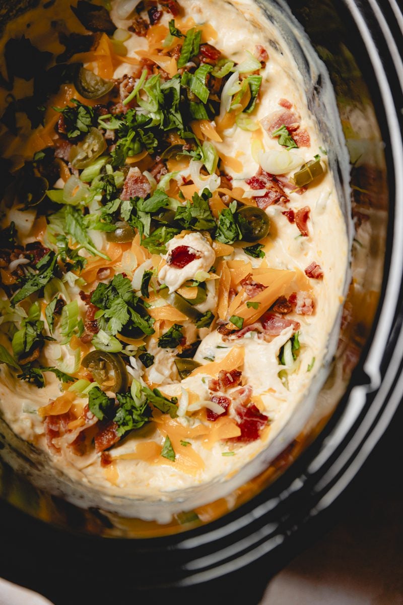 Jalapeno popper dip in a crockpot garnished with green onions and bacon.