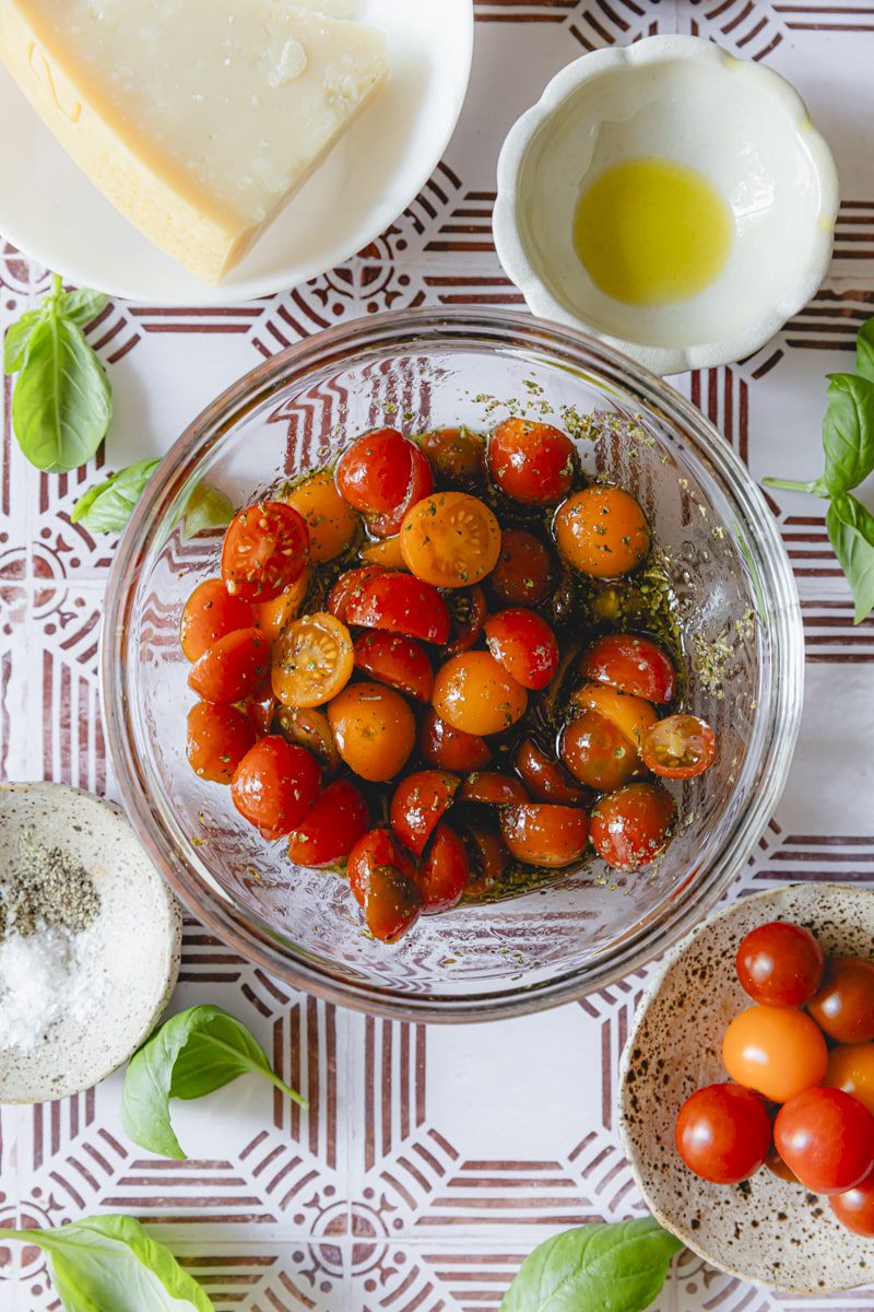 All ingredients for the Italian tomato salad stirred together in a glass bowl. 