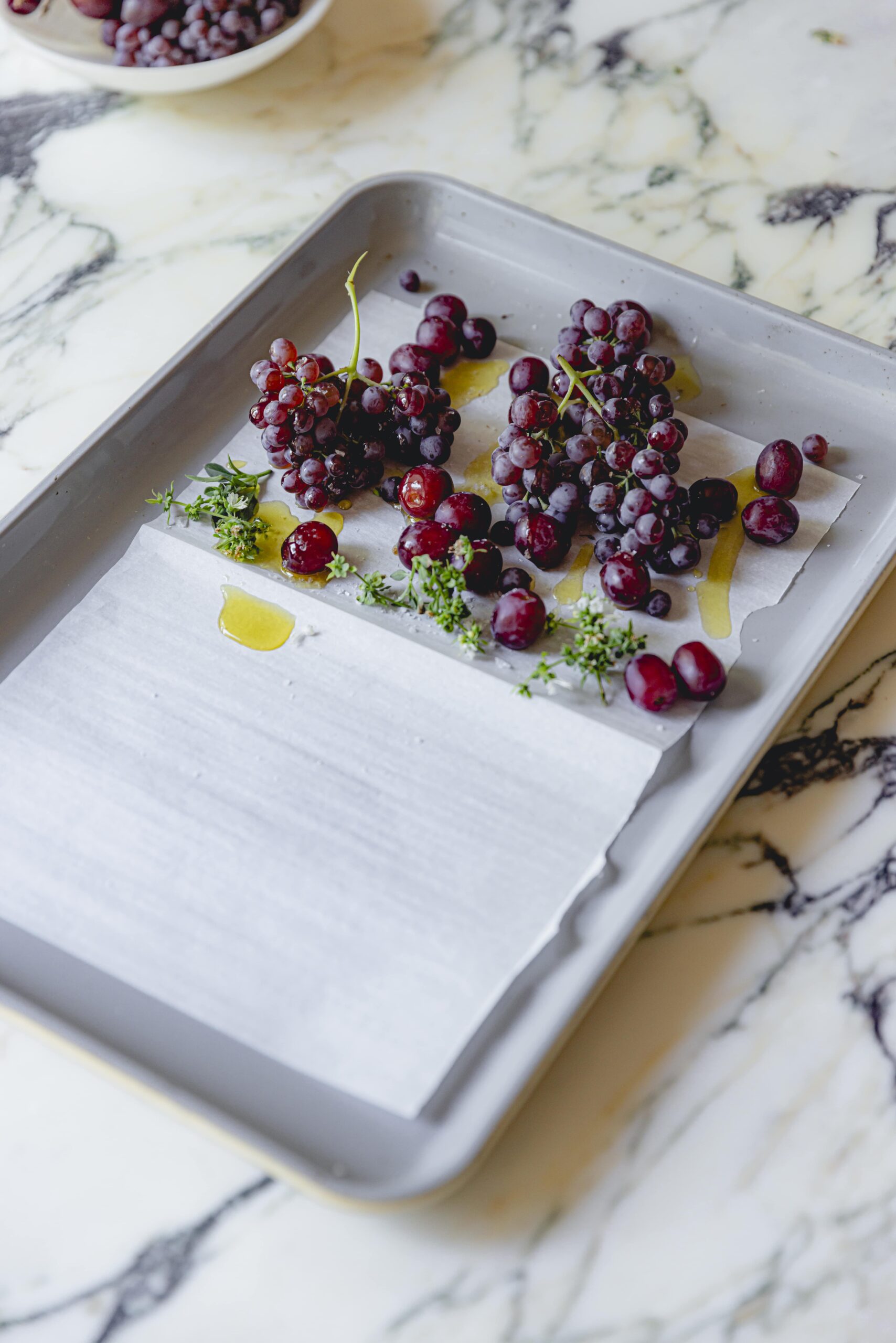 Grapes and thyme on a sheet tray with olive oil. 