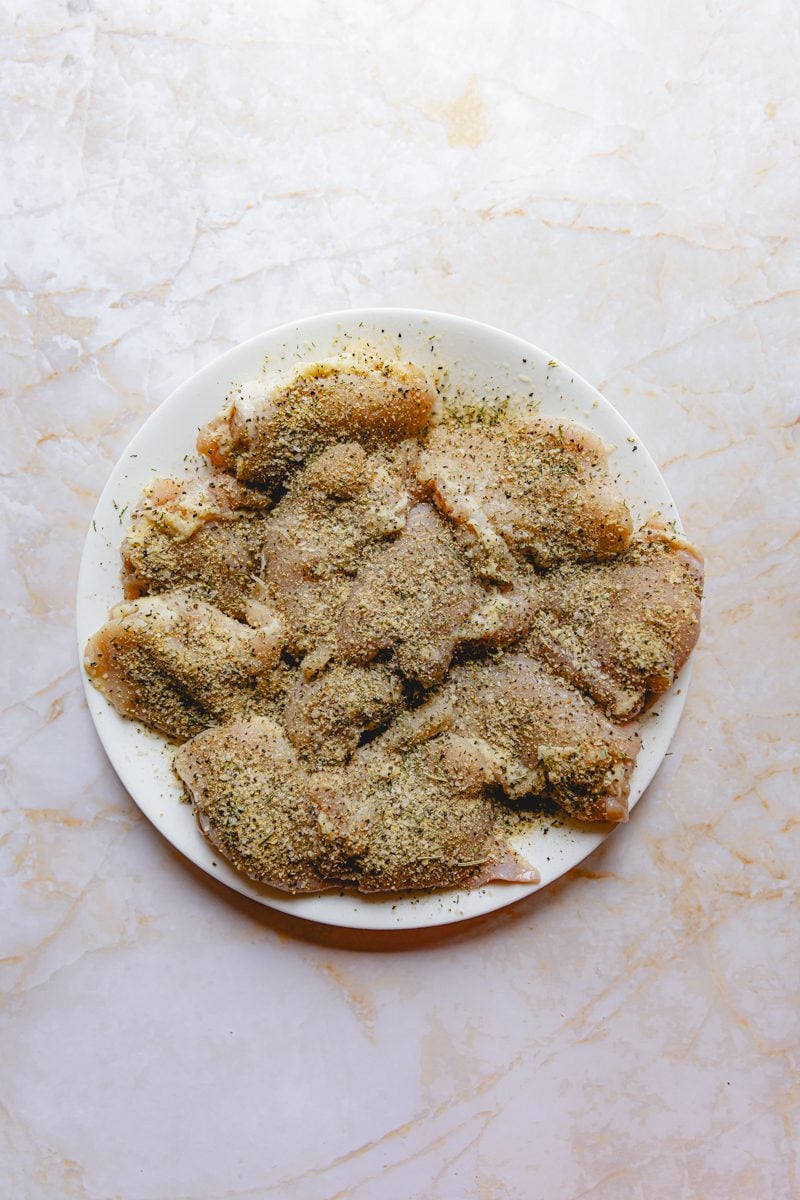 Raw, seasoned chicken on a white plate. 