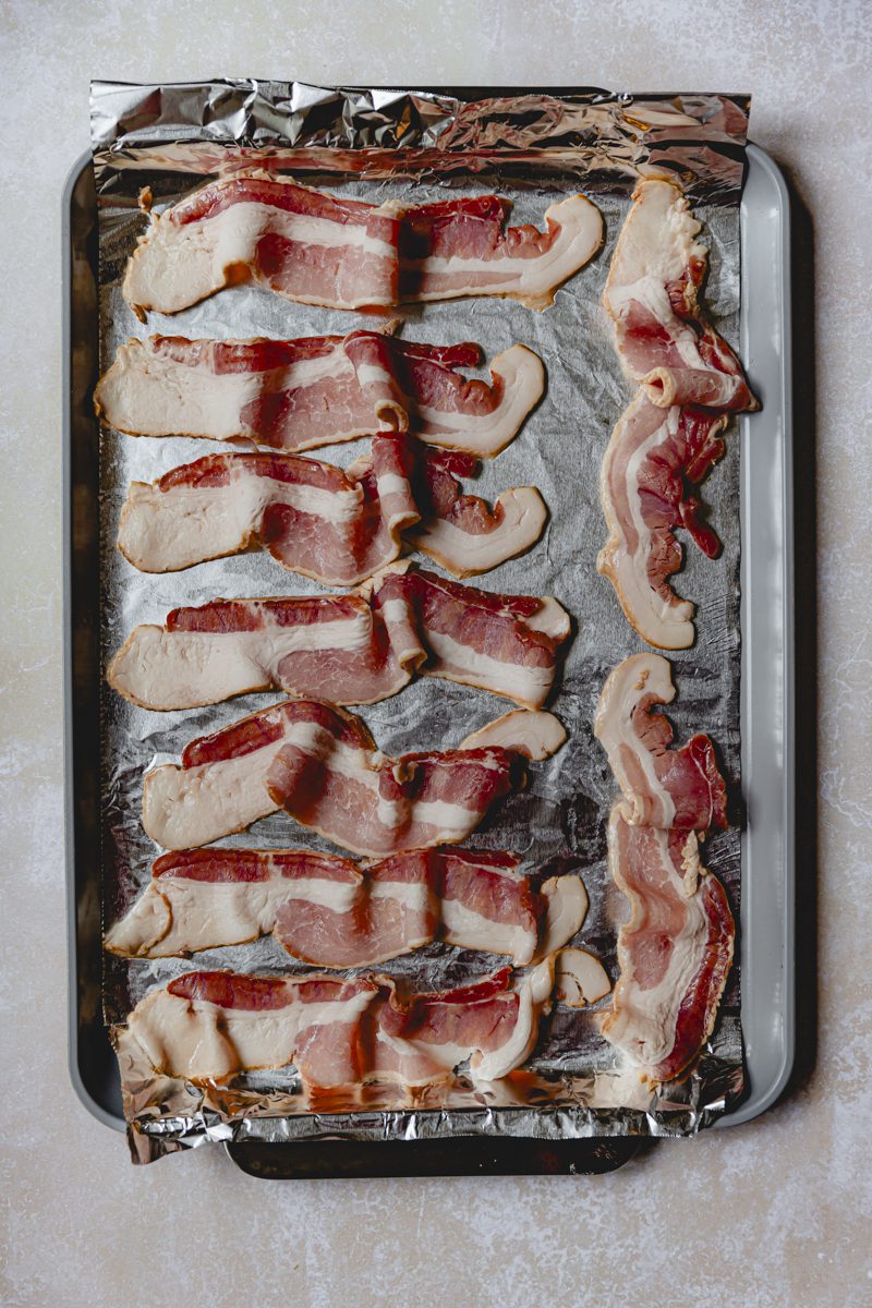 Raw bacon on foil lined sheet tray. 
