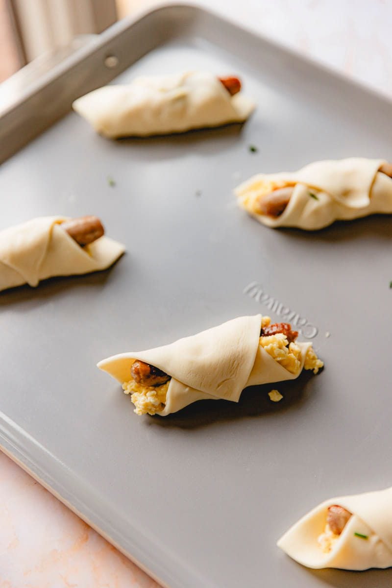 Puff pastry sausage and egg sandwiches rolled up on a sheet pan.