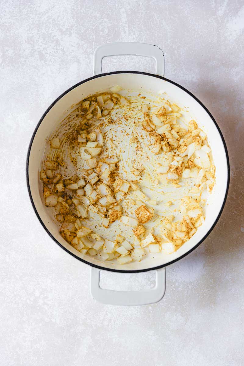 Sautรฉing onion in a white skillet.