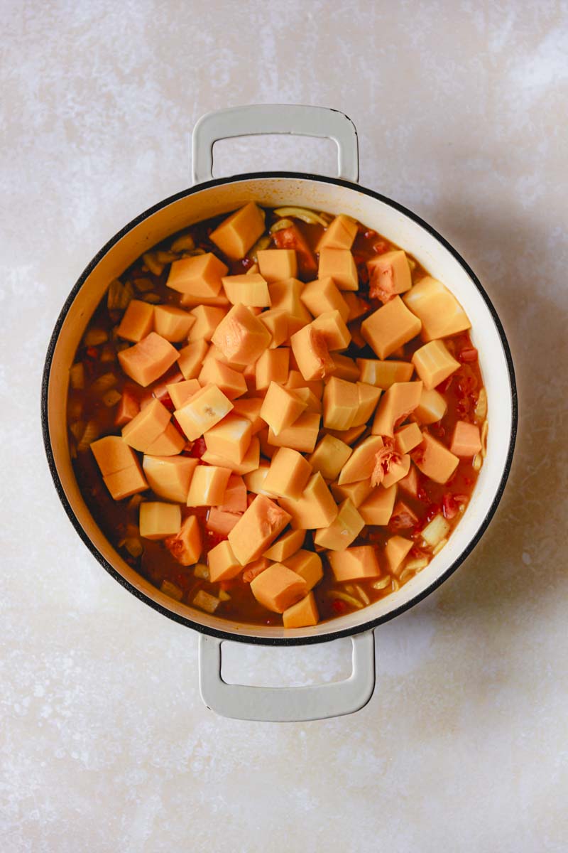 Tomatoes, squash,nsweet potato, and chicken broth in a white skillet.