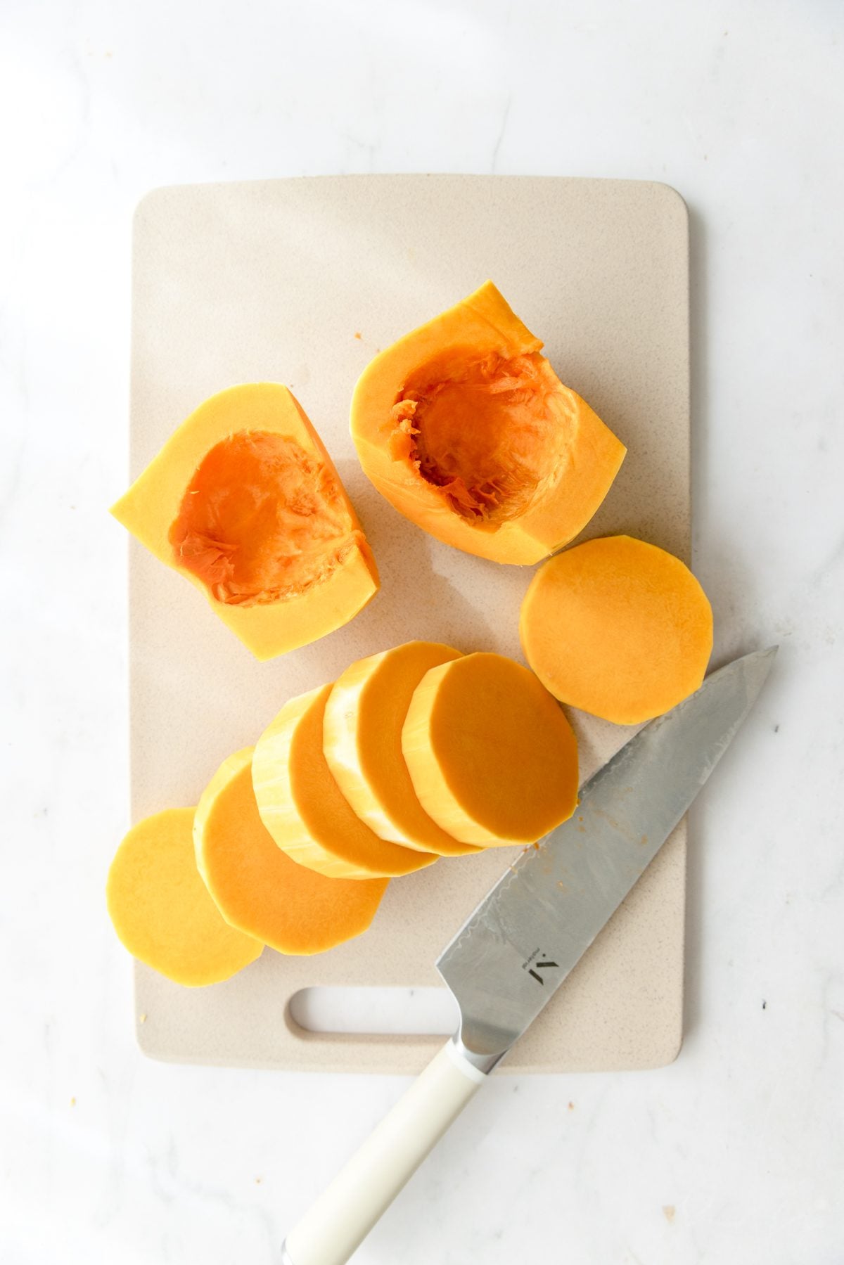 Cut butternut squash half moons on a cutting board with a knife.