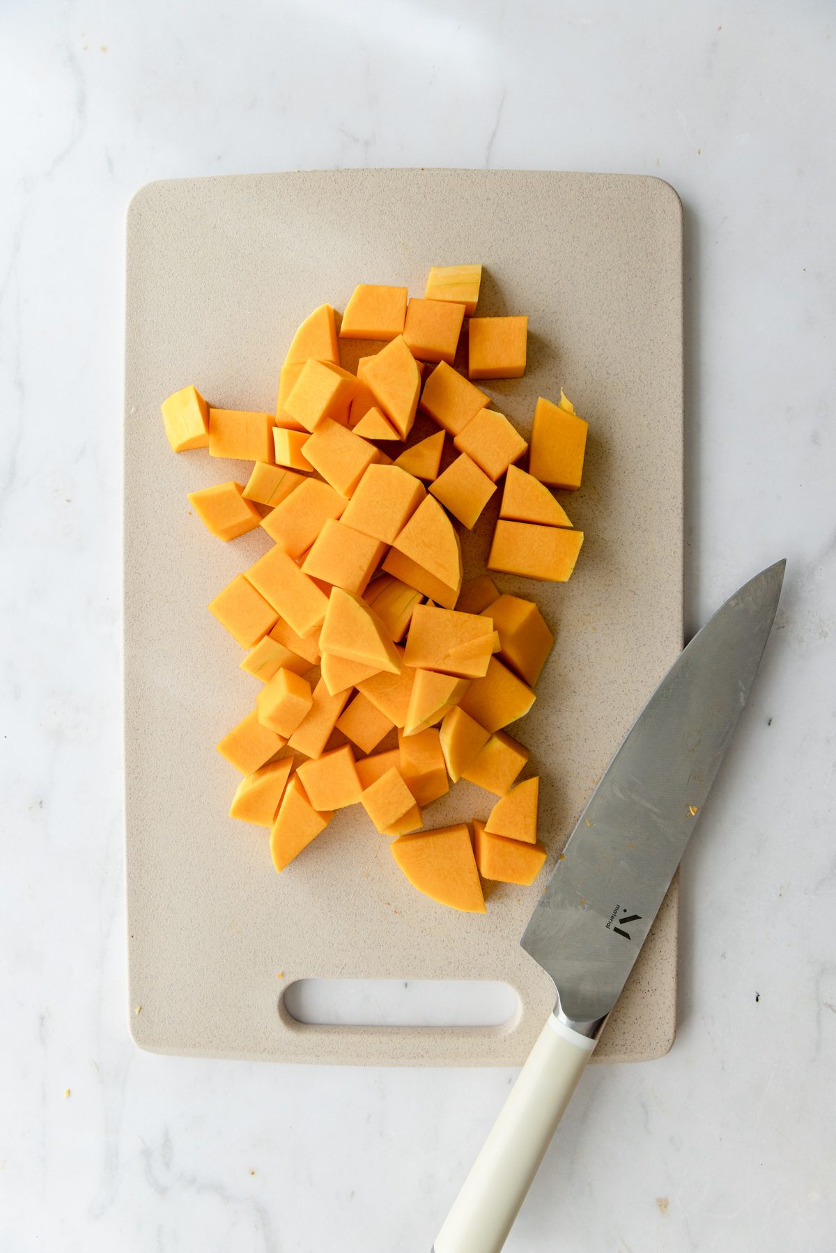 Cubed butternut squash on a cutting board with a knife.
