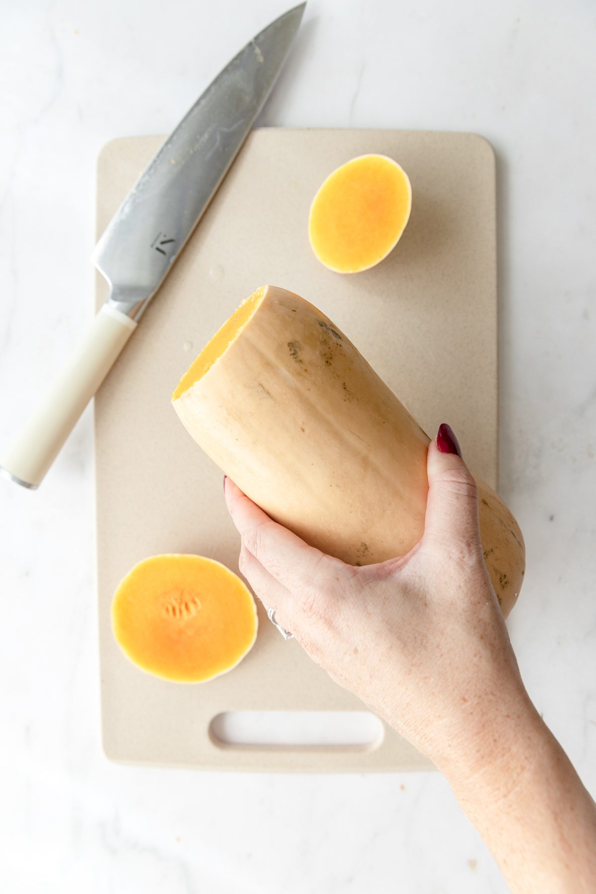 A butternut squash with the ends trimmed off over a cutting board.